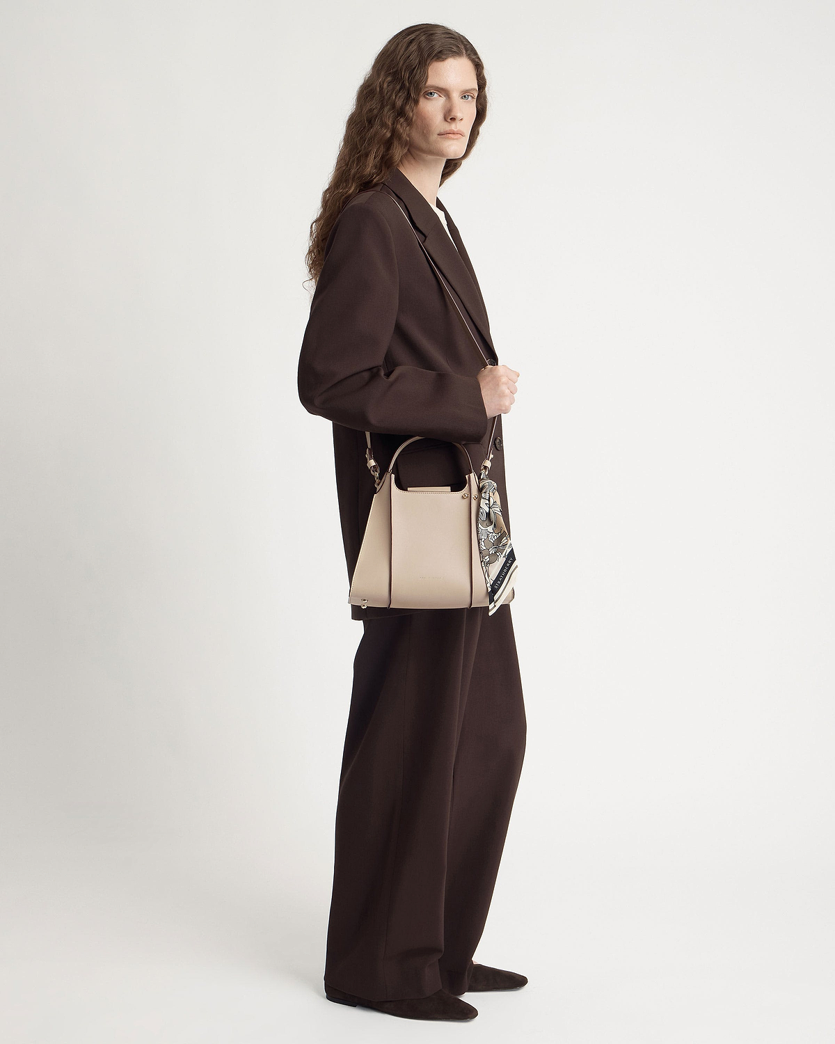 Model in brown suit holding an oat-coloured structured leather handbag with silk scarf.
