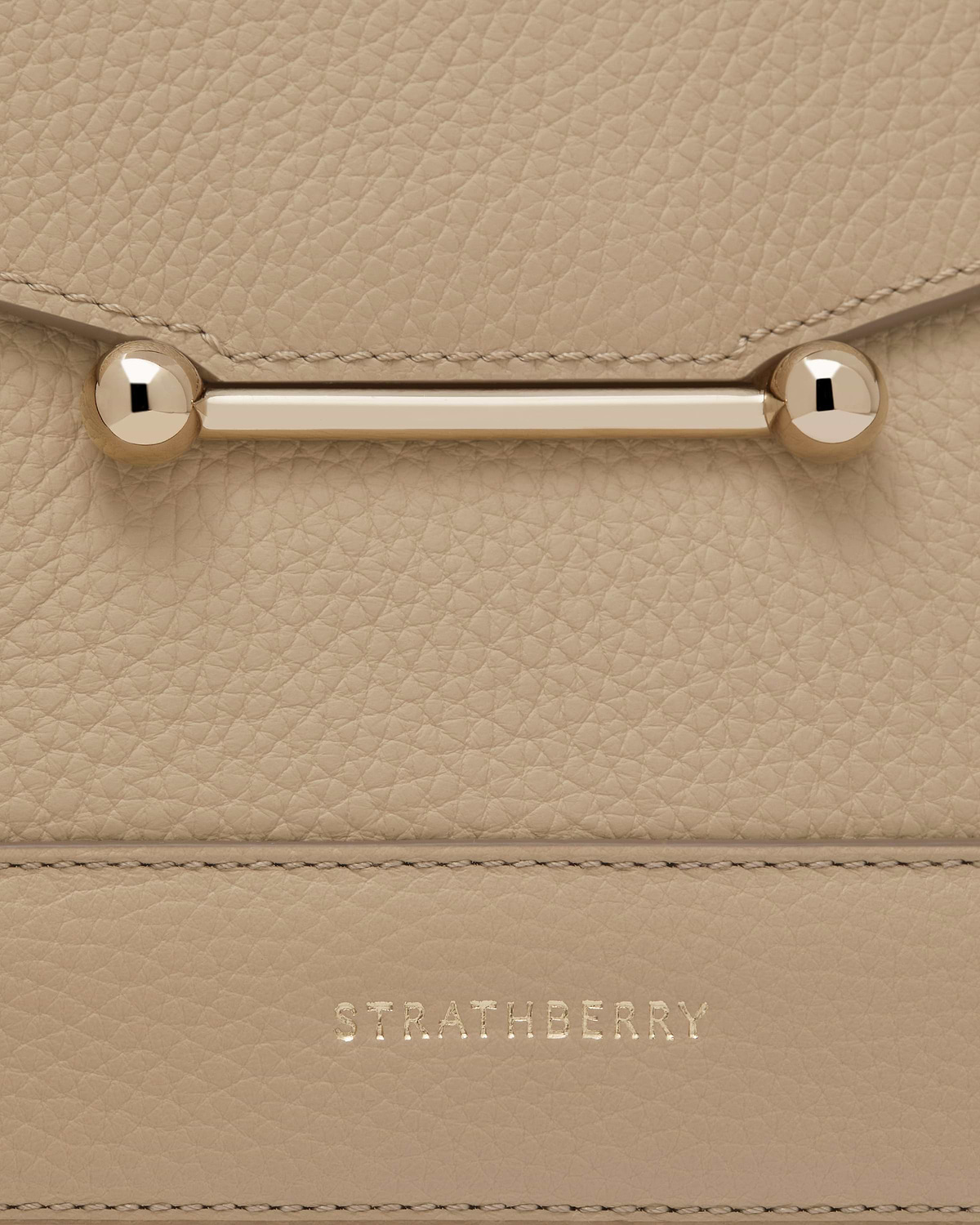 Close-up of sand mosaic bag leather, gold bar clasp and Strathberry logo.