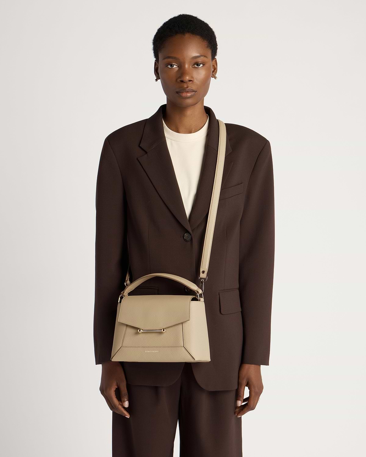 Model wearing brown blazer carrying sand mosaic bag by Strathberry with shoulder strap.