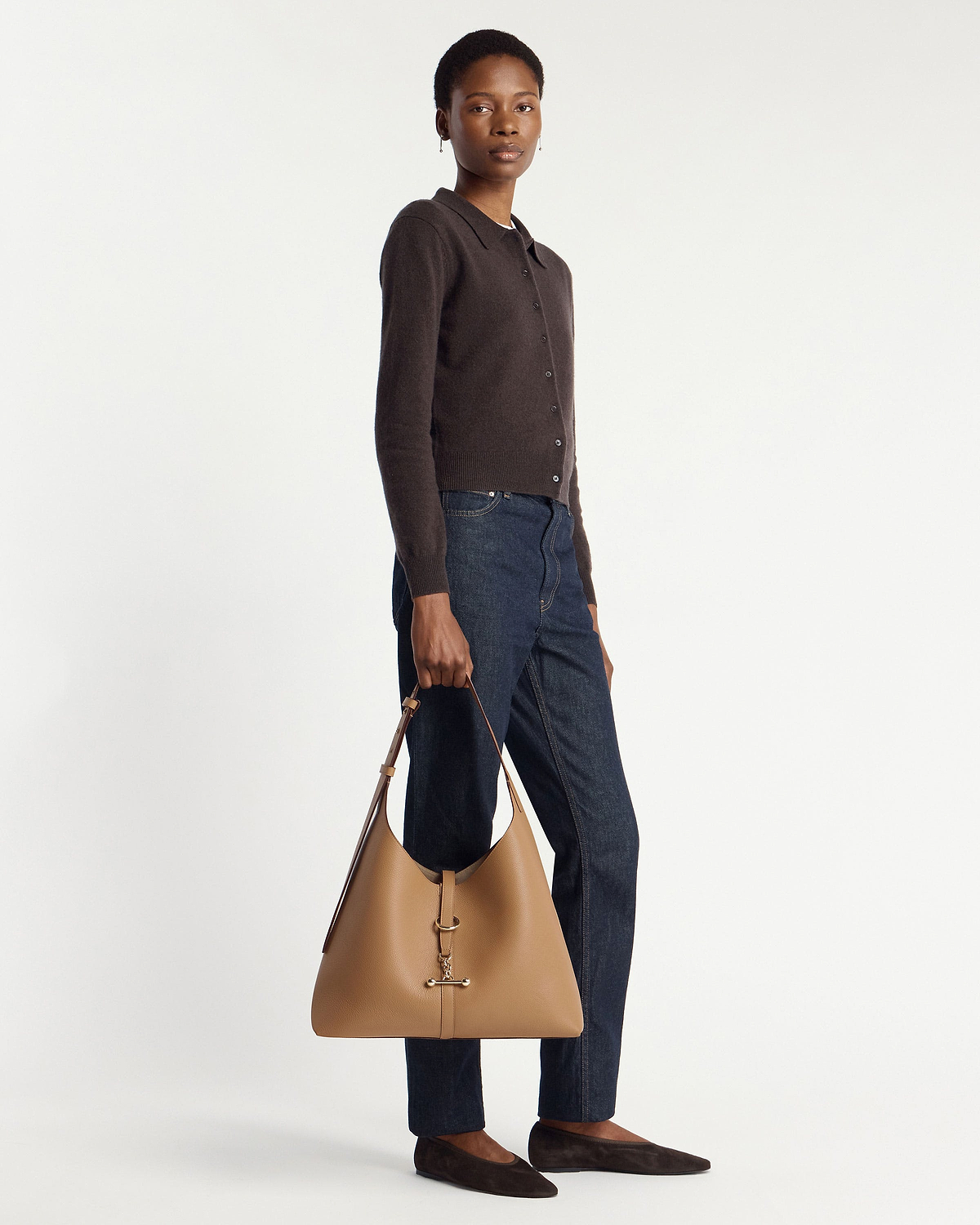 Model holding a caramel hobo bag with gold hardware, wearing cardigan and jeans.