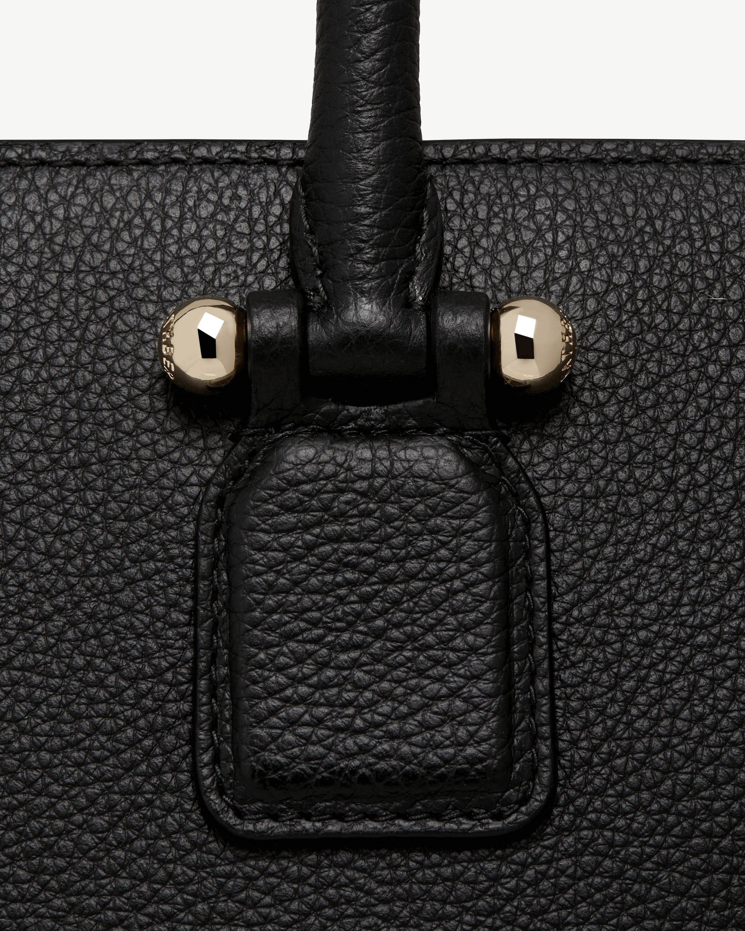 Close-up of black pebbled leather bag handle attachment with two gold studs.