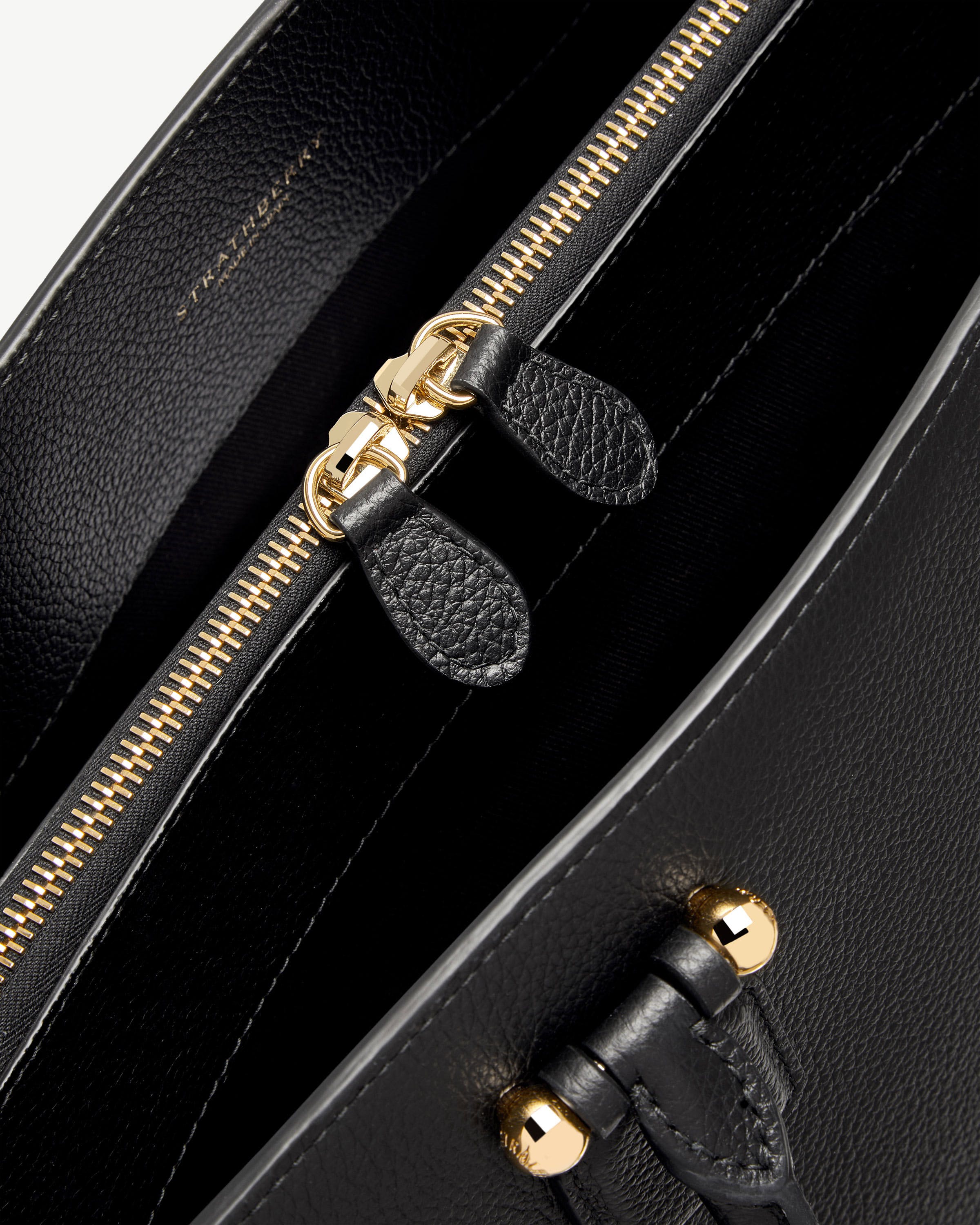 Close-up of black Strathberry bag interior showing gold zip and leather pull tabs.