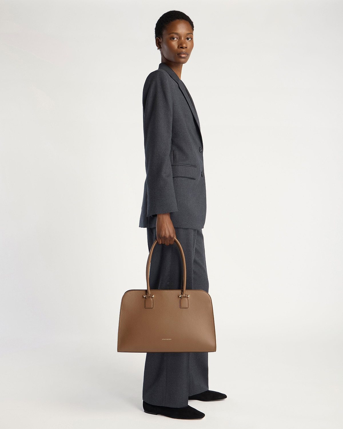 Model holding clay Georgia Maxi handbag by Strathberry, full-length view.