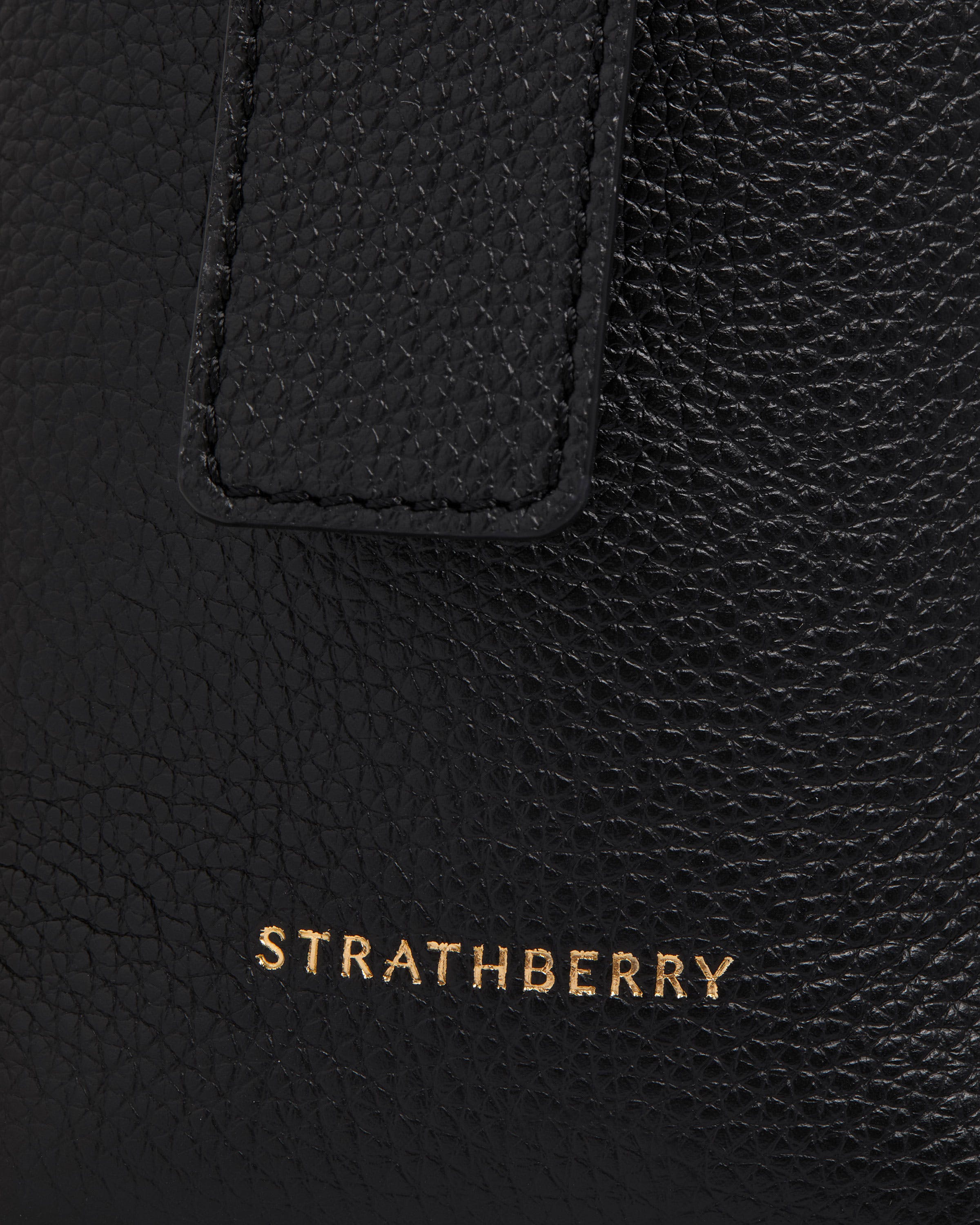 Black leather bag detail showing pebbled texture and gold Strathberry logo