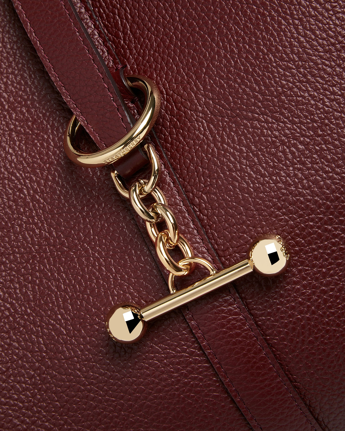 Oxblood pebbled leather strap with gold chain hardware and Strathberry logo.