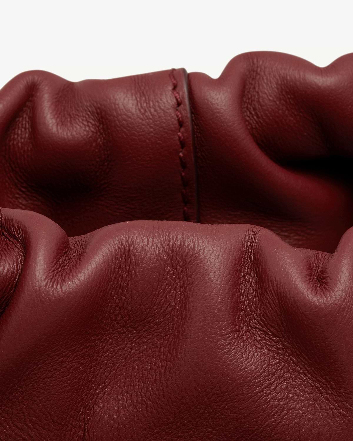 Oxblood leather drawstring bag with gathered top and visible central seam.