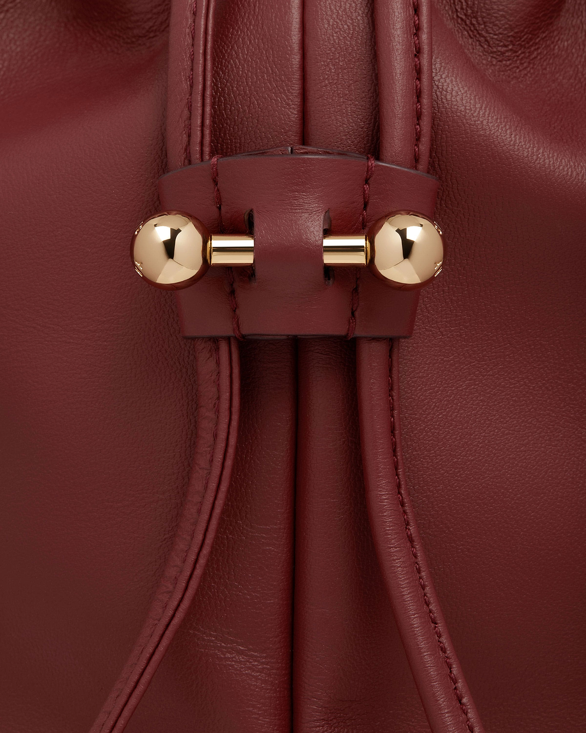 Drawstring detail of oxblood leather bag with gold bar and spherical ends.