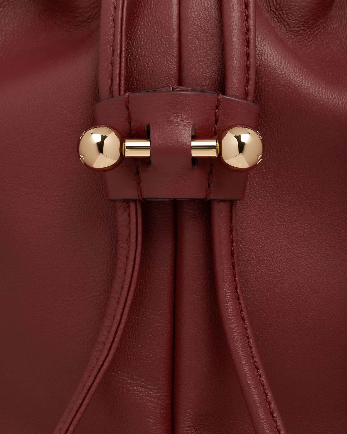 Drawstring detail of oxblood leather bag with gold bar and spherical ends.