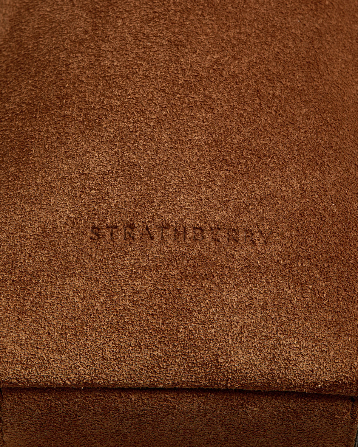 Tan suede bag flap with textured nap and faint embossed wordmark