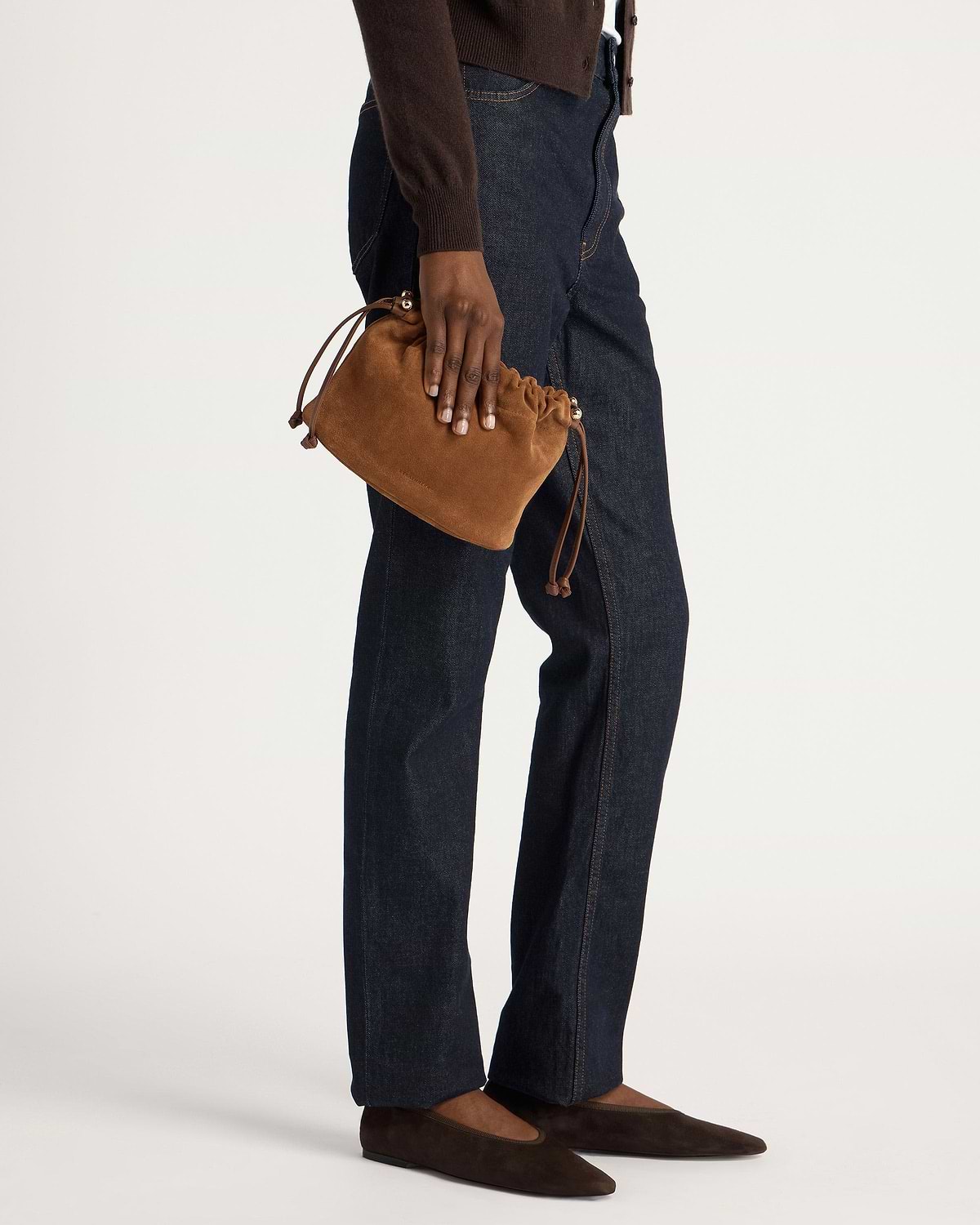 Tan suede drawstring bag held by model wearing dark jeans and brown flats.