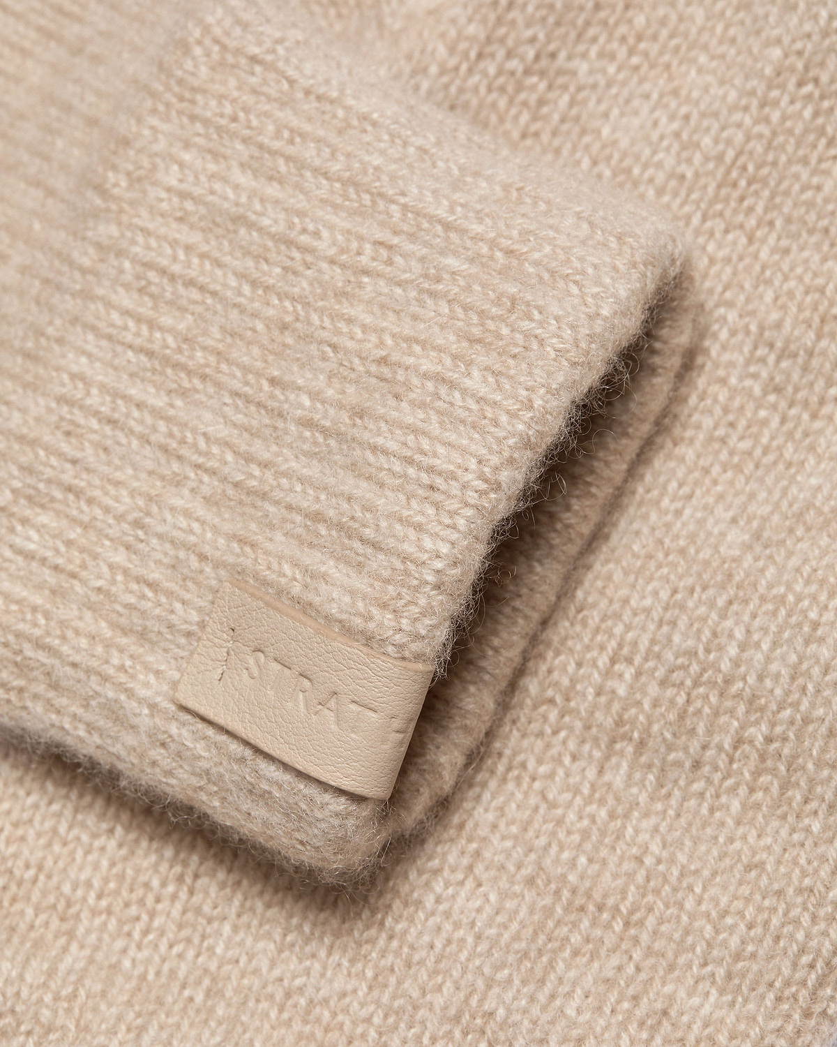 Oat-coloured fingerless cashmere glove showing knit texture and leather tag
