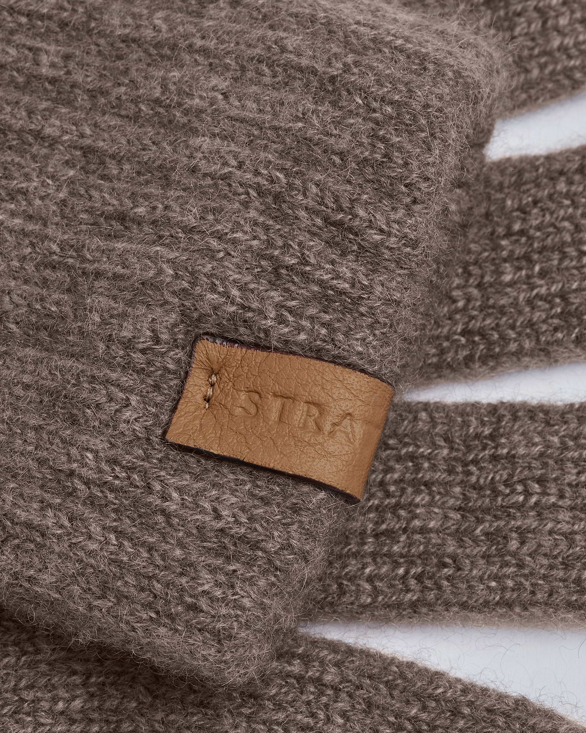 Close-up of otter-colour cashmere Westray gloves showing leather Strathberry label.