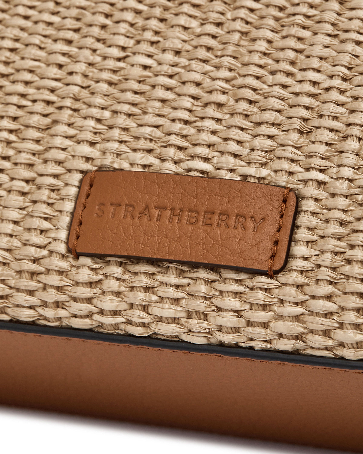 Tan leather patch embossed 'Strathberry' on natural raffia weave, mini tote detail.