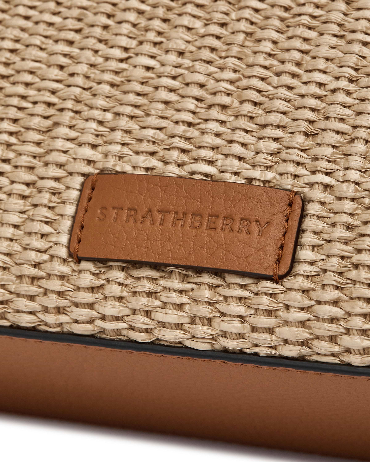 Tan leather patch embossed 'Strathberry' on natural raffia weave, mini tote detail.