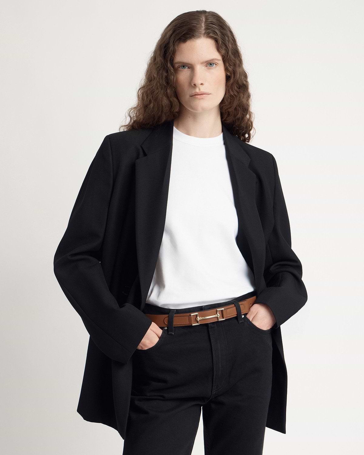 Model wearing a tan leather belt with gold hardware, black blazer and white t-shirt.