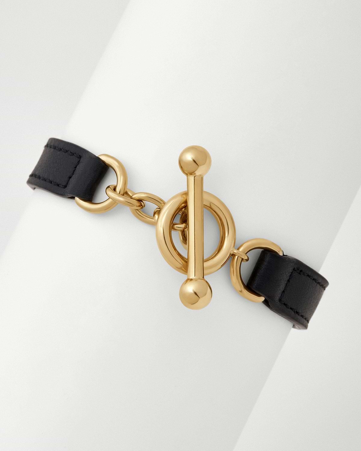 Close-up of black leather kite bracelet showing polished gold toggle clasp and chain.