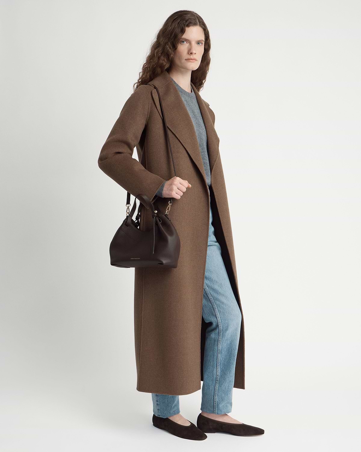 Model wearing long brown coat and jeans holding espresso leather Barra Mini bag.