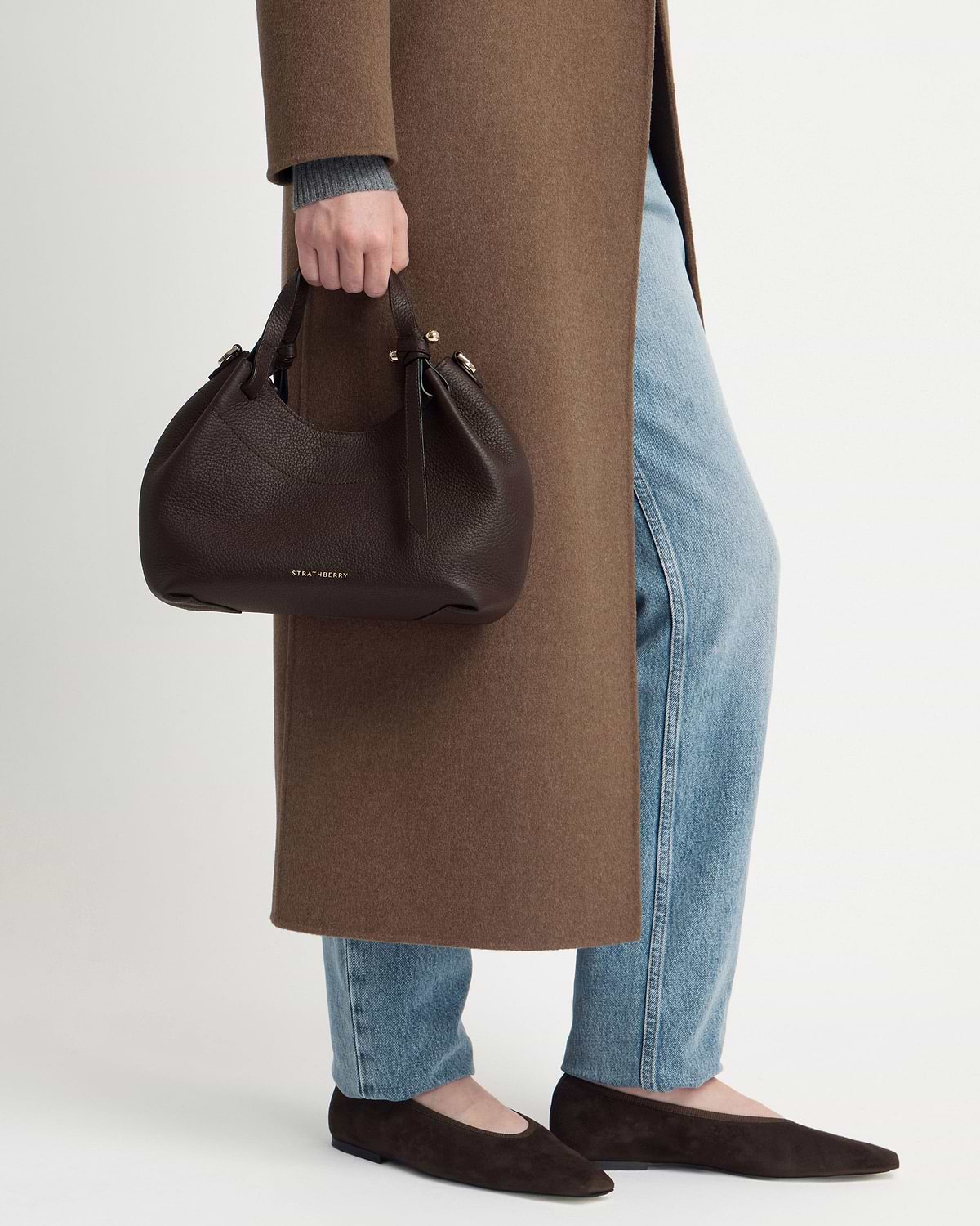 Model holding Strathberry Barra Mini bag in espresso with gold logo.