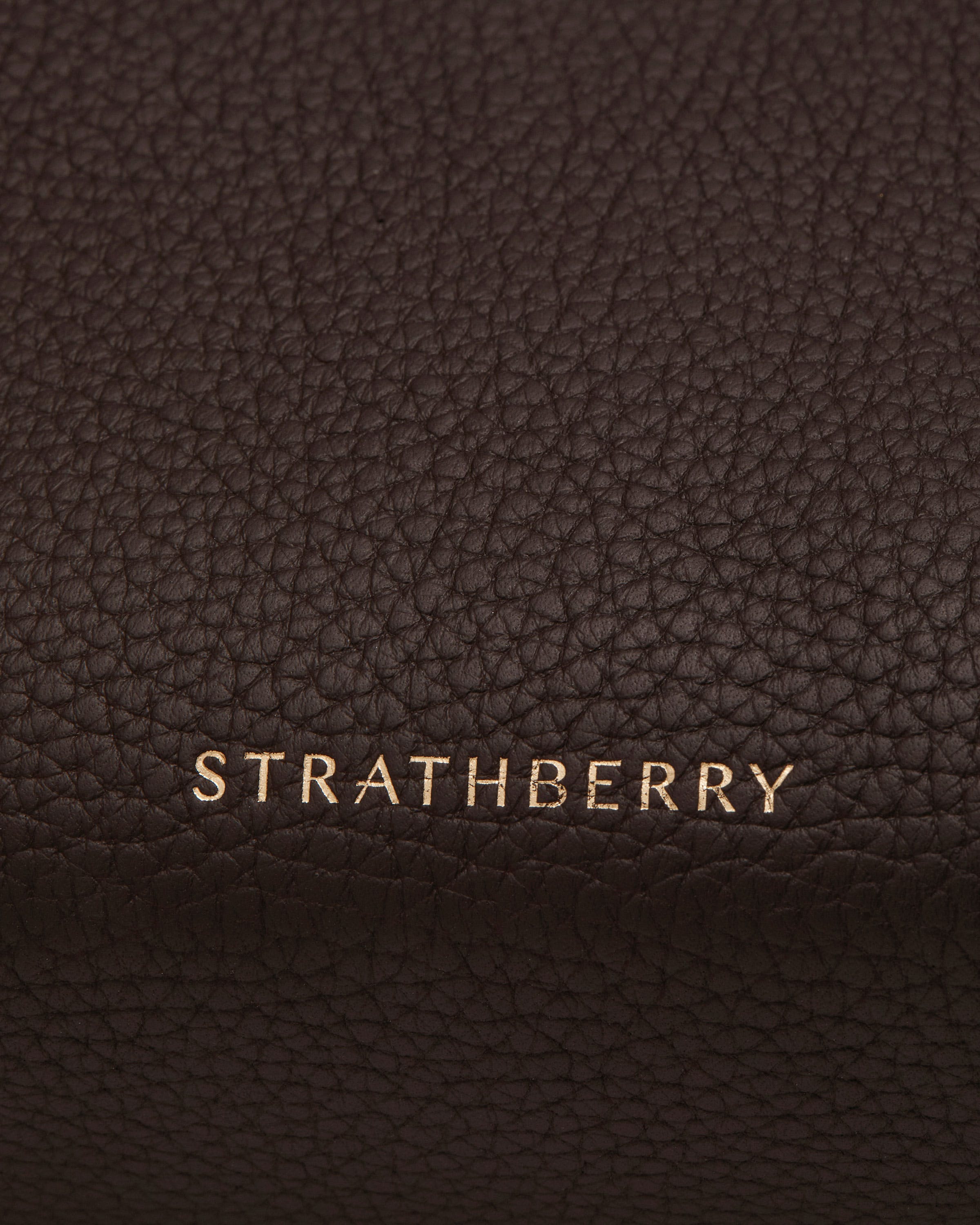 Gold Strathberry logo on espresso pebbled leather of a bag.