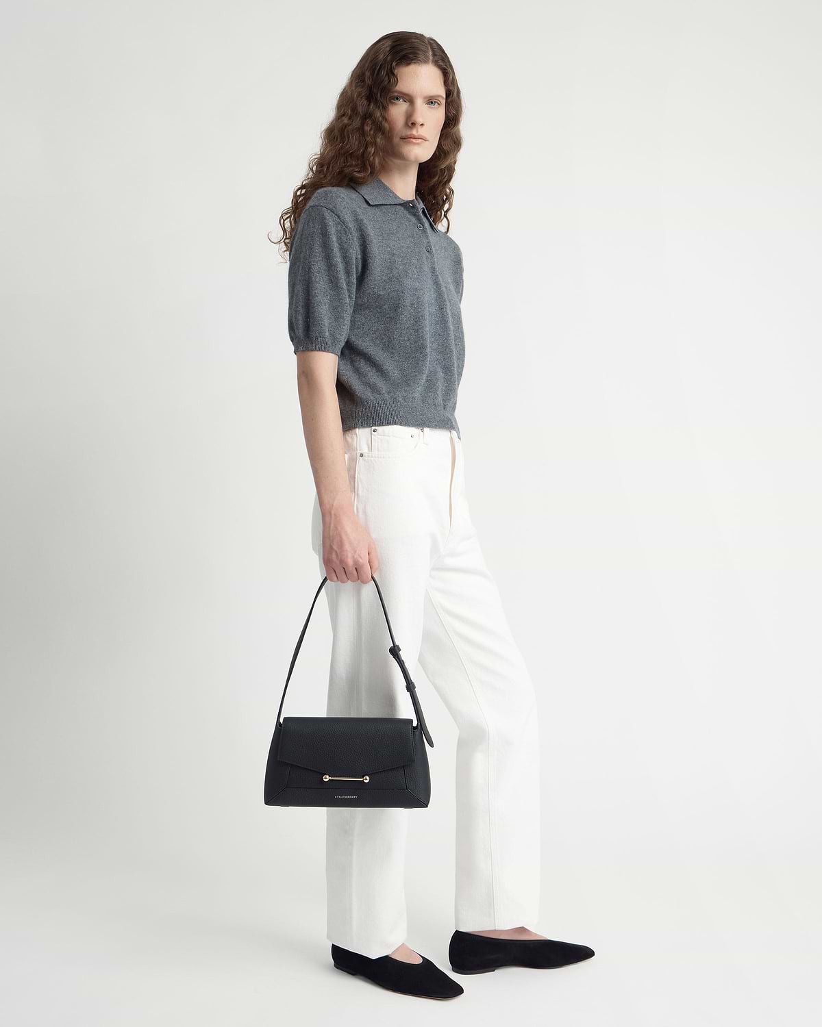 Model in grey top and white trousers holding a black Mosaic shoulder bag.