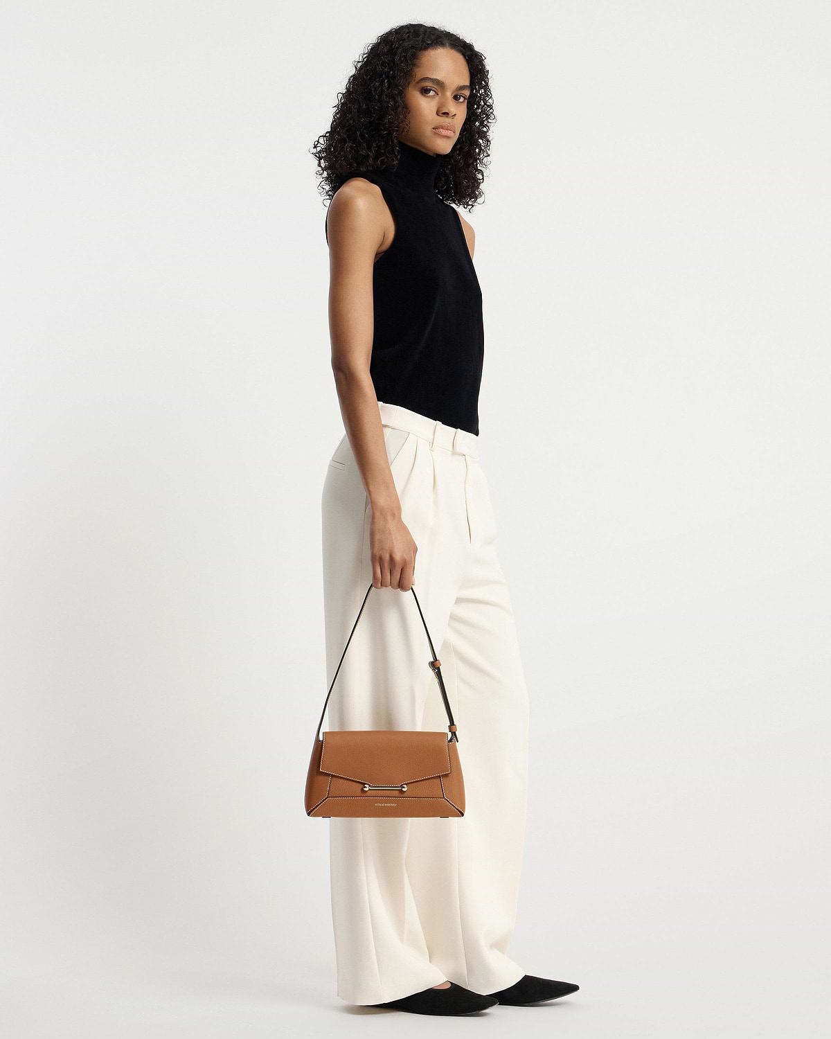 Model holding tan Strathberry Mosaic Shoulder bag by top handle.