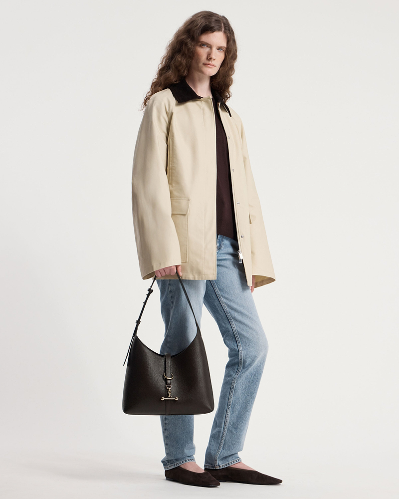 Model holding an espresso leather Kite Hobo shoulder bag by the strap.