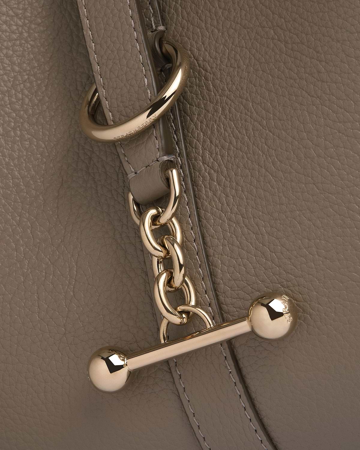 Taupe pebbled leather with gold chain hardware and engraved Strathberry metal ring.