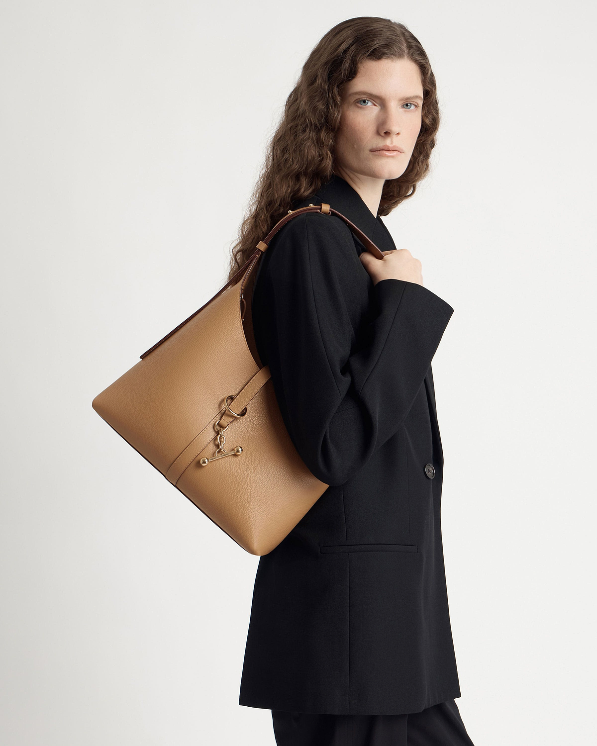 Woman in black blazer carrying caramel Kite Hobo shoulder bag over her shoulder.