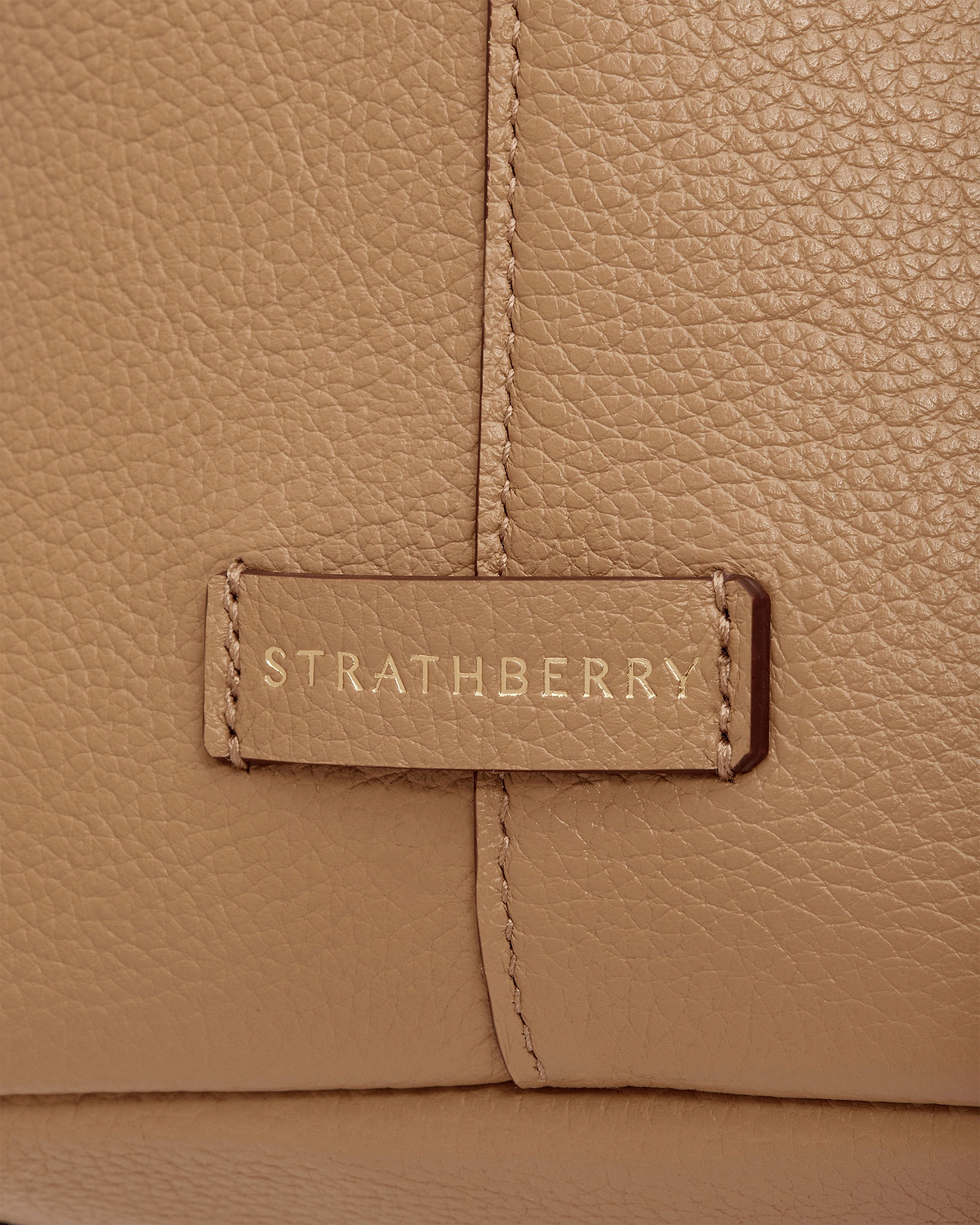 Caramel pebbled leather detail showing Strathberry logo on stitched tab of tote.