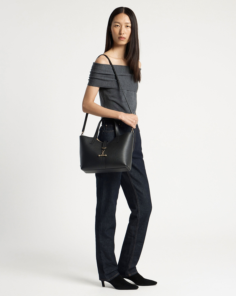 Model wearing grey off-shoulder top and dark jeans carrying black tote bag.
