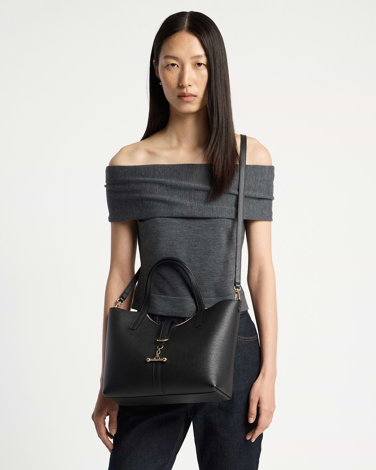 Woman wearing off-shoulder top carries black Kite Tote Midi with gold bar clasp.