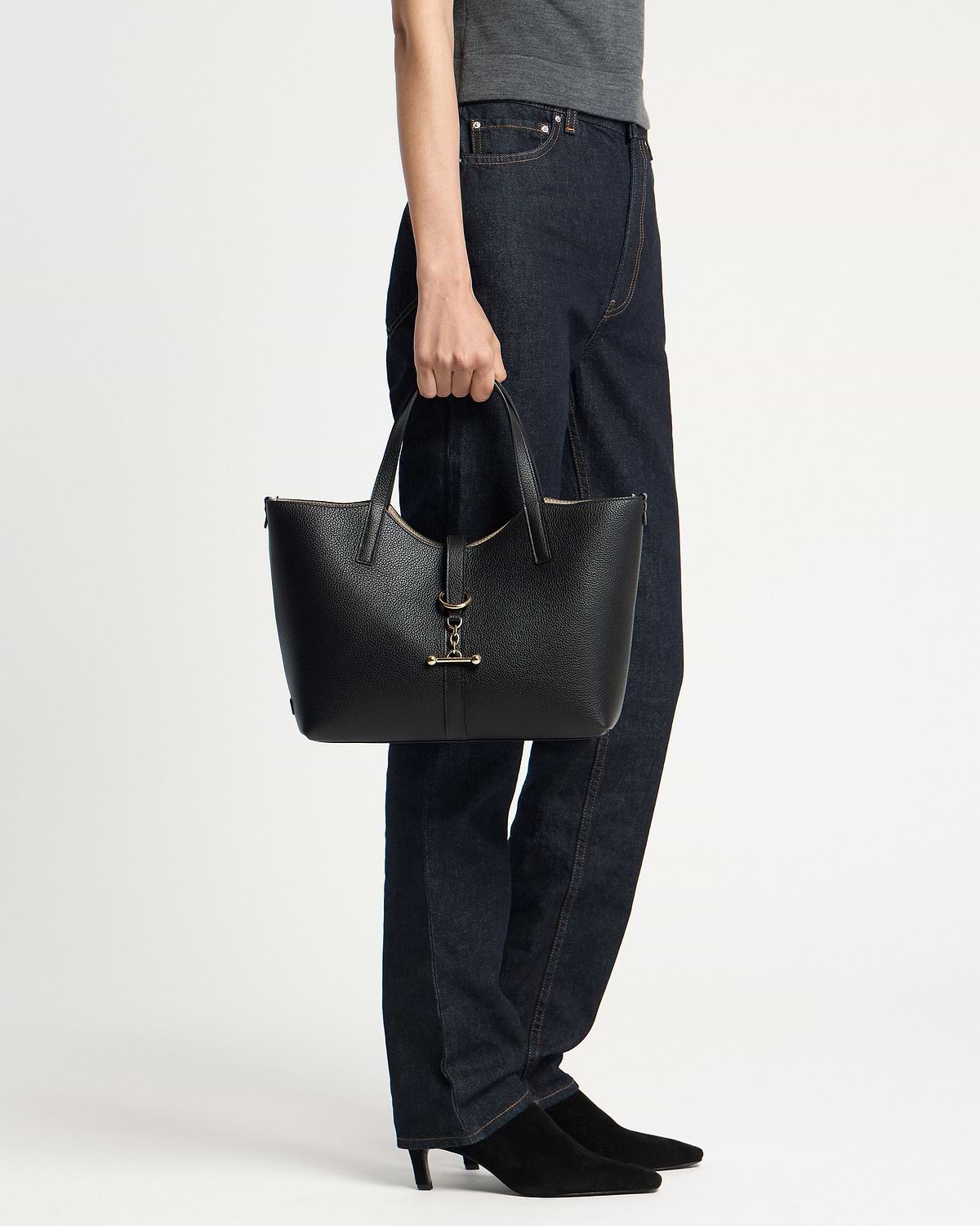 Model holding black pebbled leather tote bag with gold bar hardware by its handles
