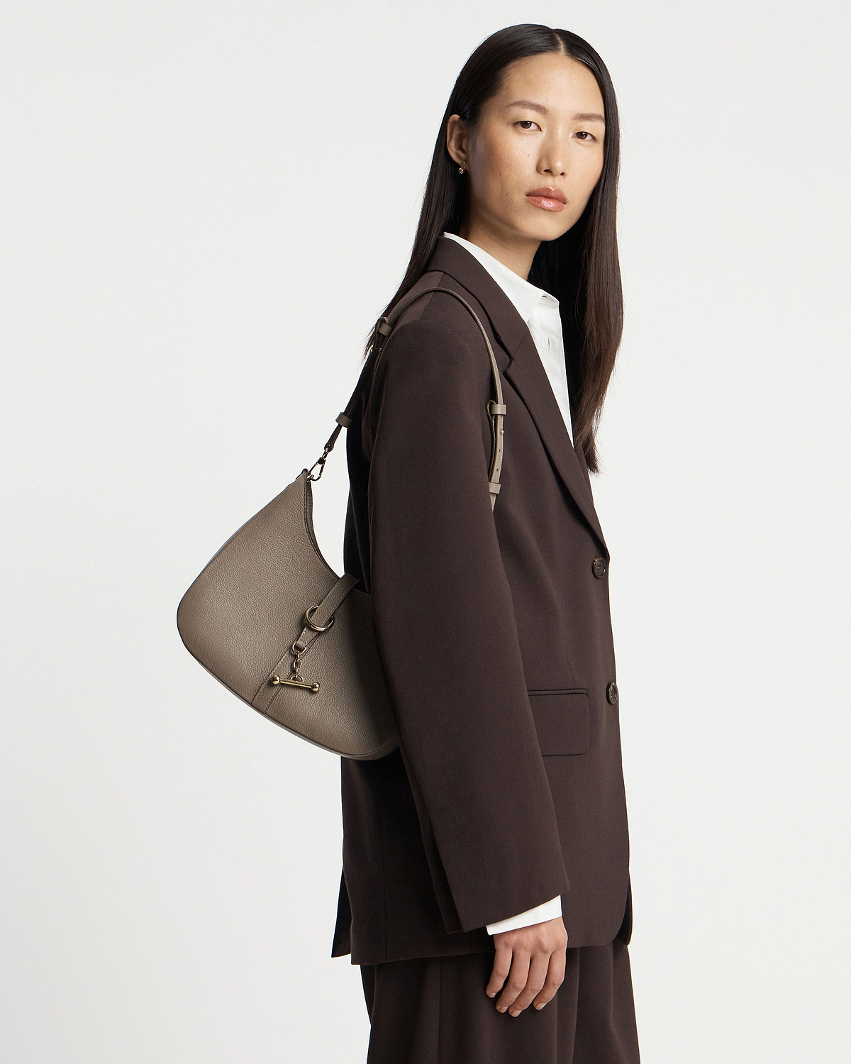 Model wearing a taupe Kite Sling bag over a dark brown blazer.