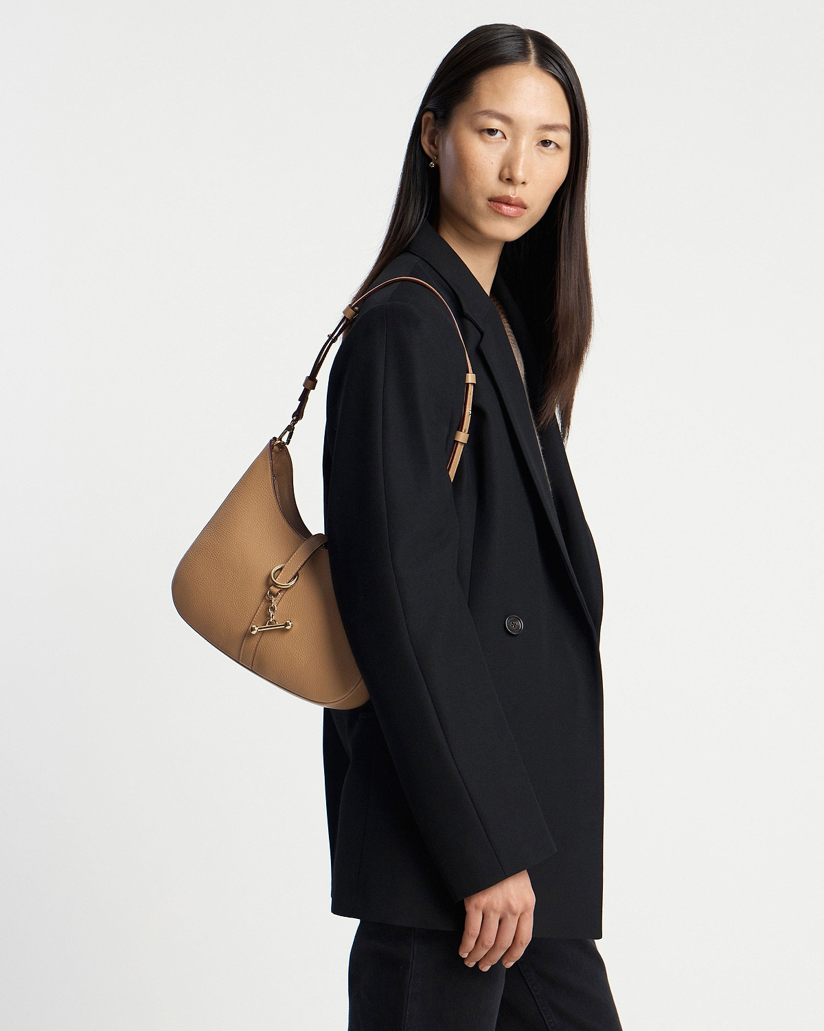 Model wearing a caramel leather kite sling bag over a black blazer.