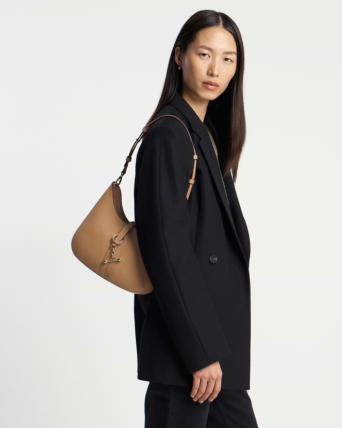 Model wearing a caramel leather kite sling bag over a black blazer.