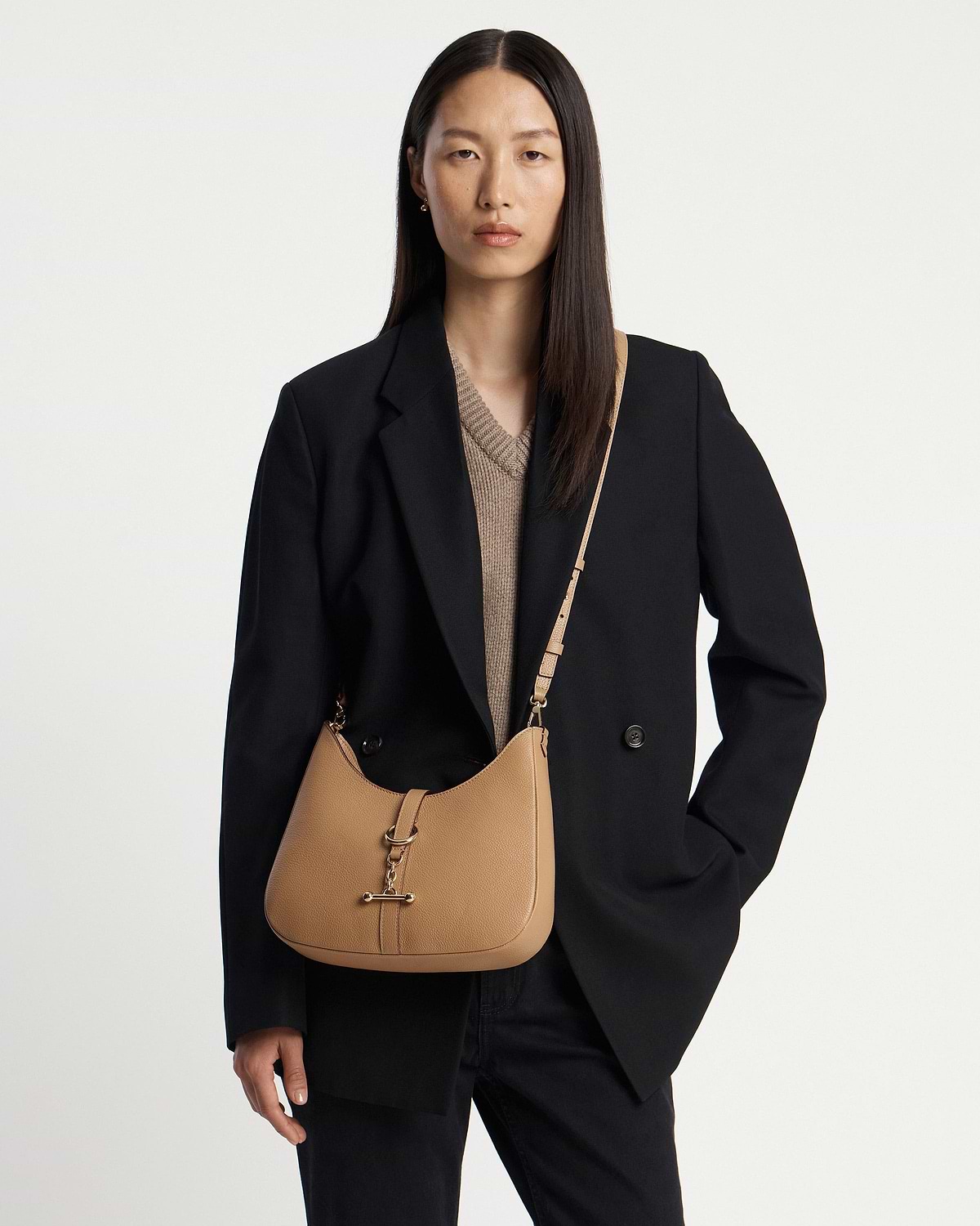 Model wearing a caramel kite sling bag with gold hardware and black blazer.