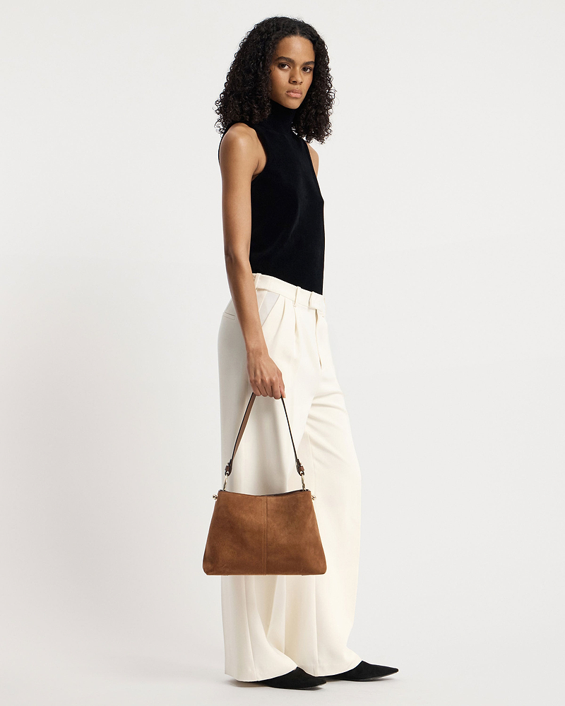 Model holding a tan suede hobo bag by its single shoulder strap.