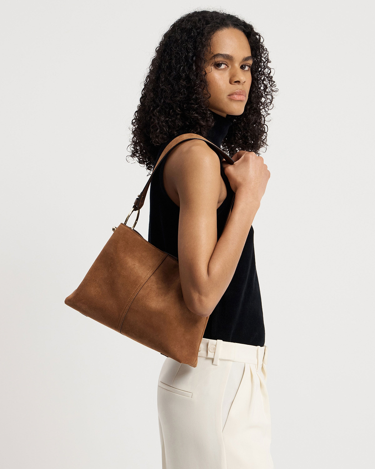 Woman wearing black sleeveless top carrying tan suede hobo bag on her shoulder.