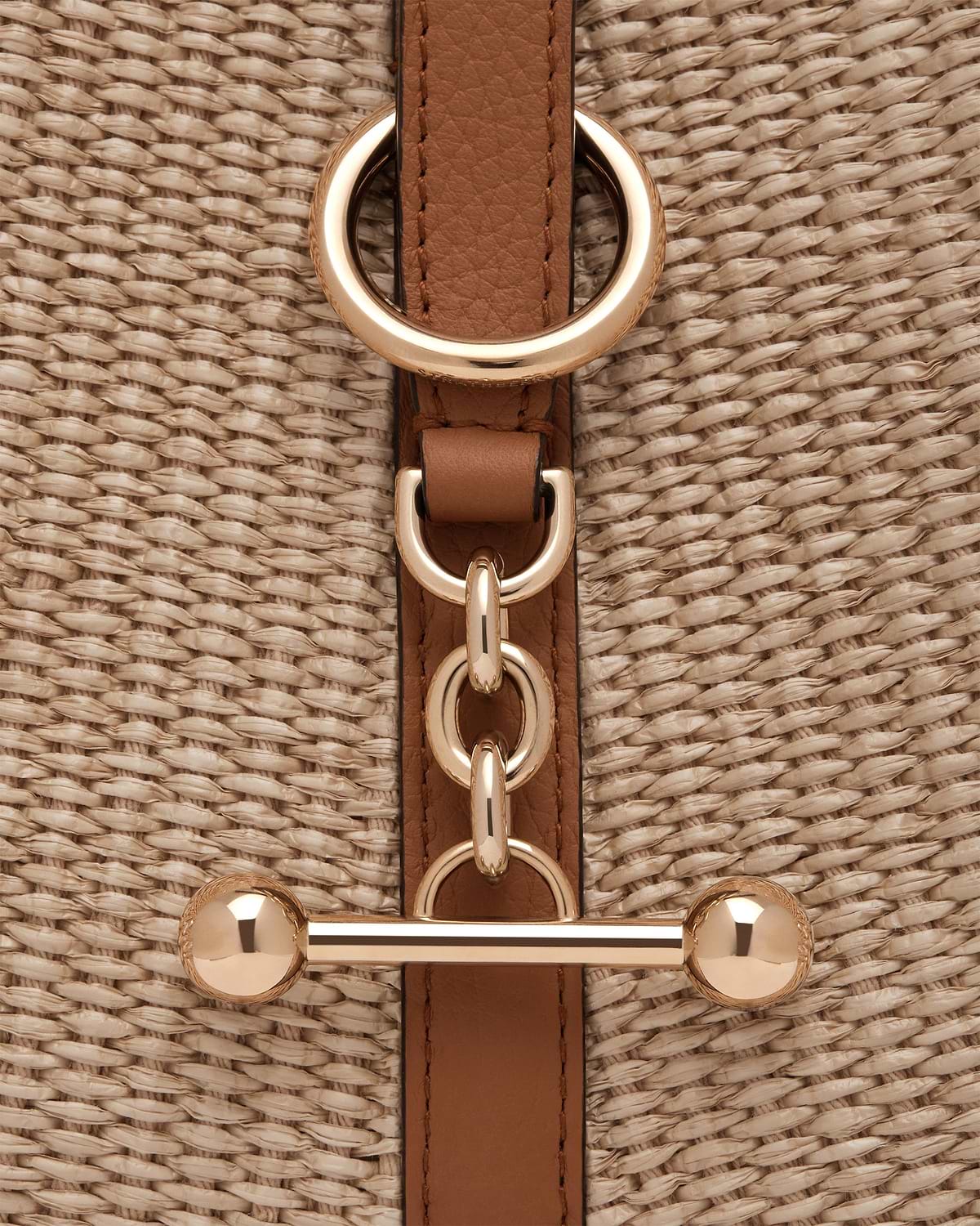 Tan leather strap with gold rings on natural raffia woven bag.