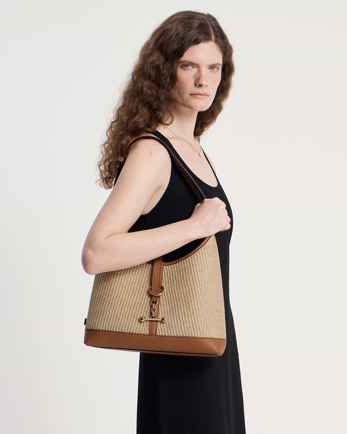 Model wearing tan natural raffia hobo bag over shoulder with leather trim.