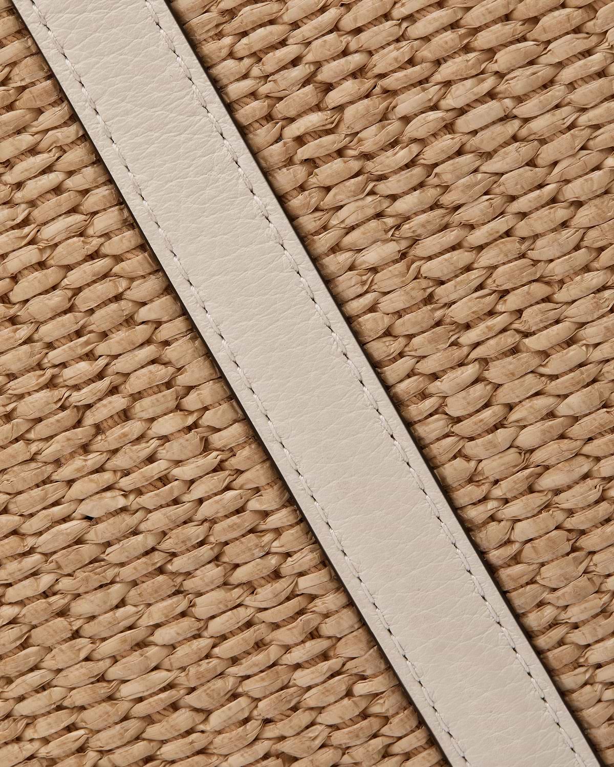 Vanilla leather strap across natural raffia weave on a hobo bag.
