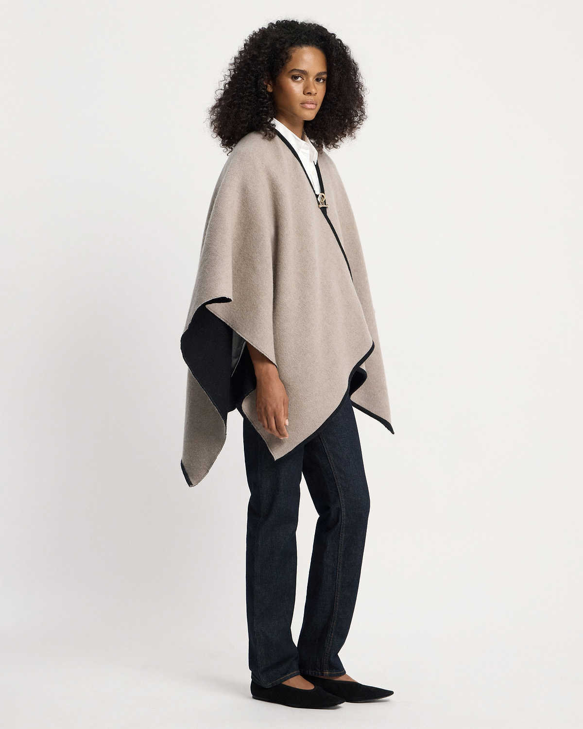 Model wearing an otter and black kite woven cape over white shirt and jeans.