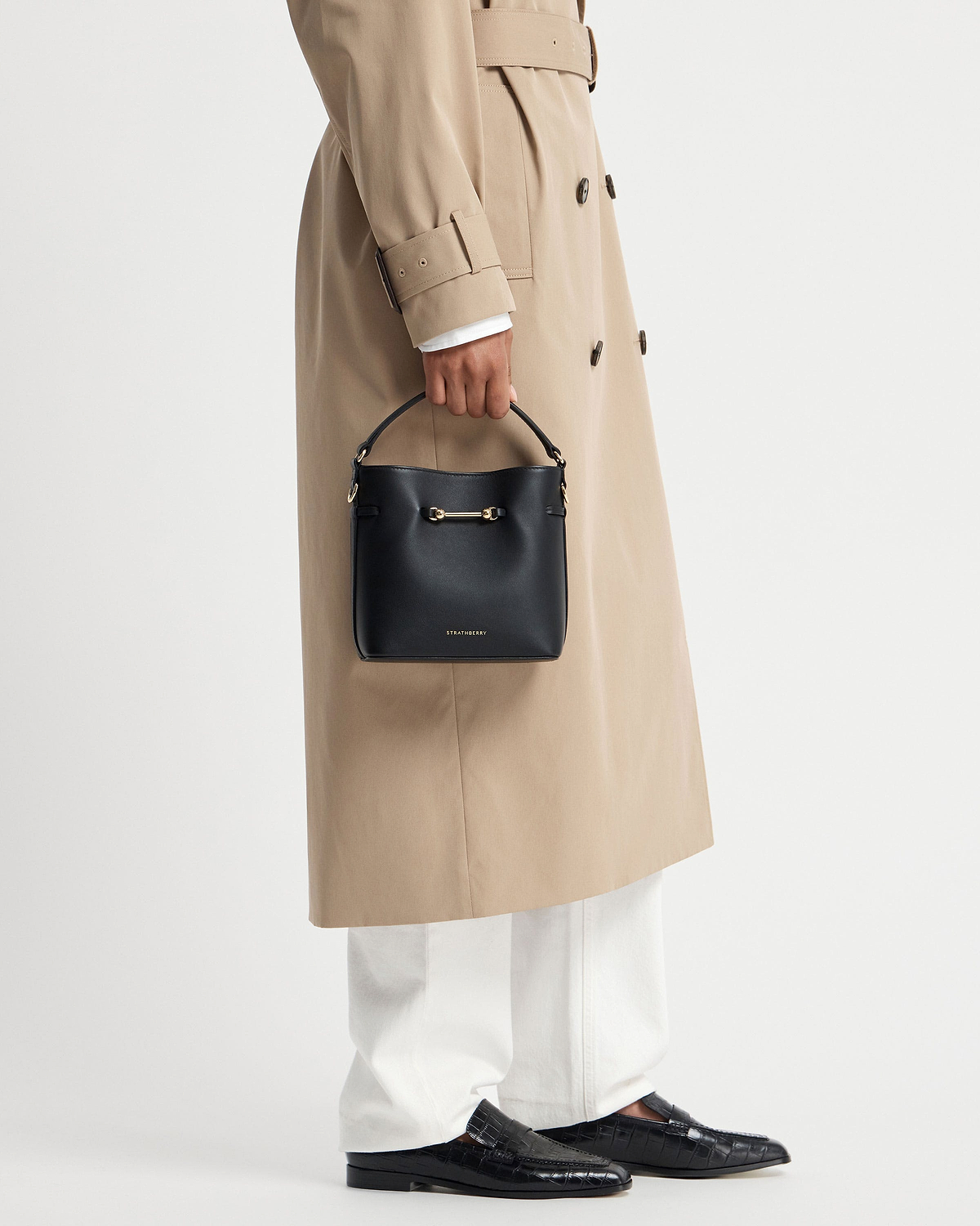 Model holding black Strathberry Corda Bucket Mini bag with beige trench coat.