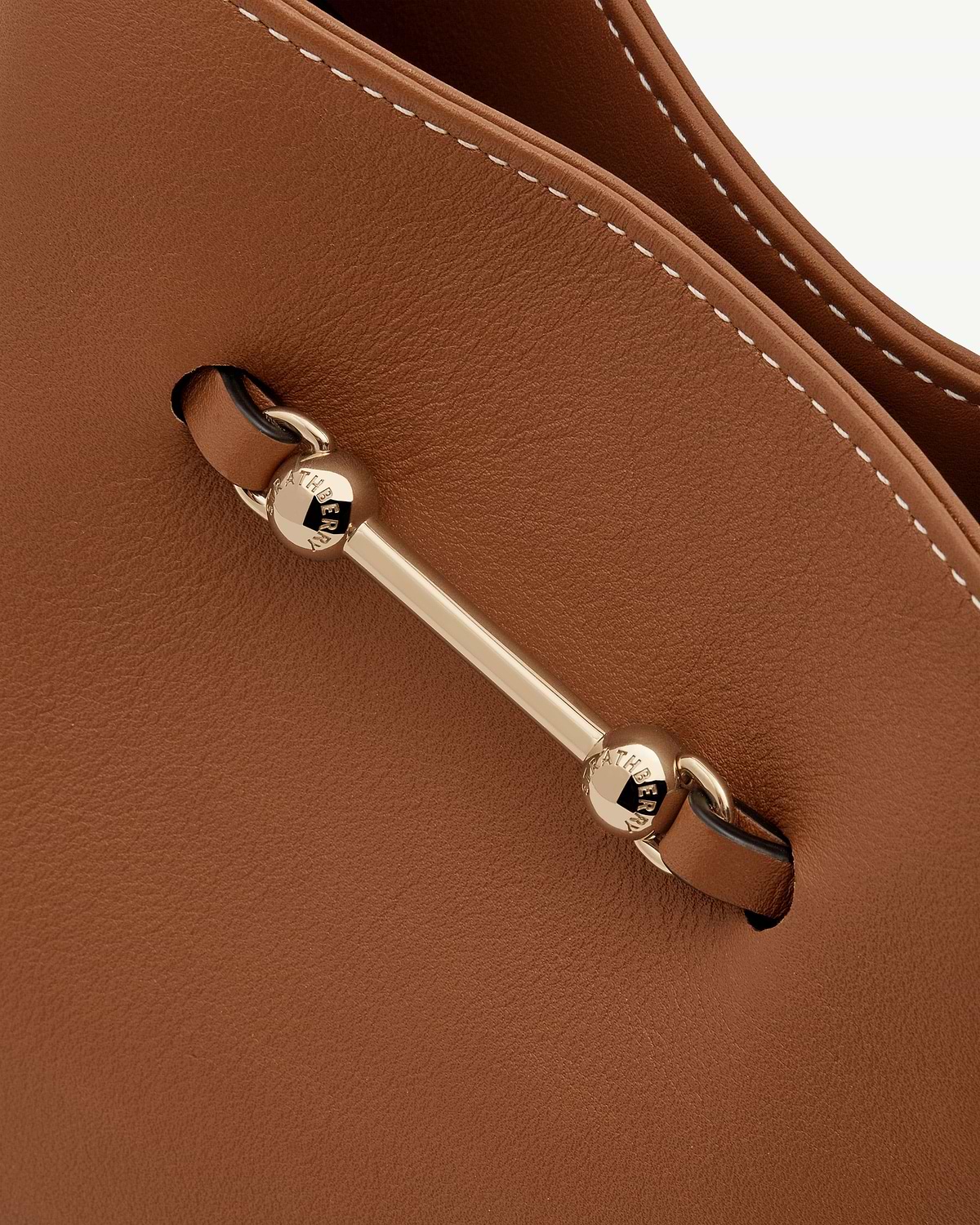 Detail of chestnut leather Strathberry bag with gold bar hardware and white stitching.
