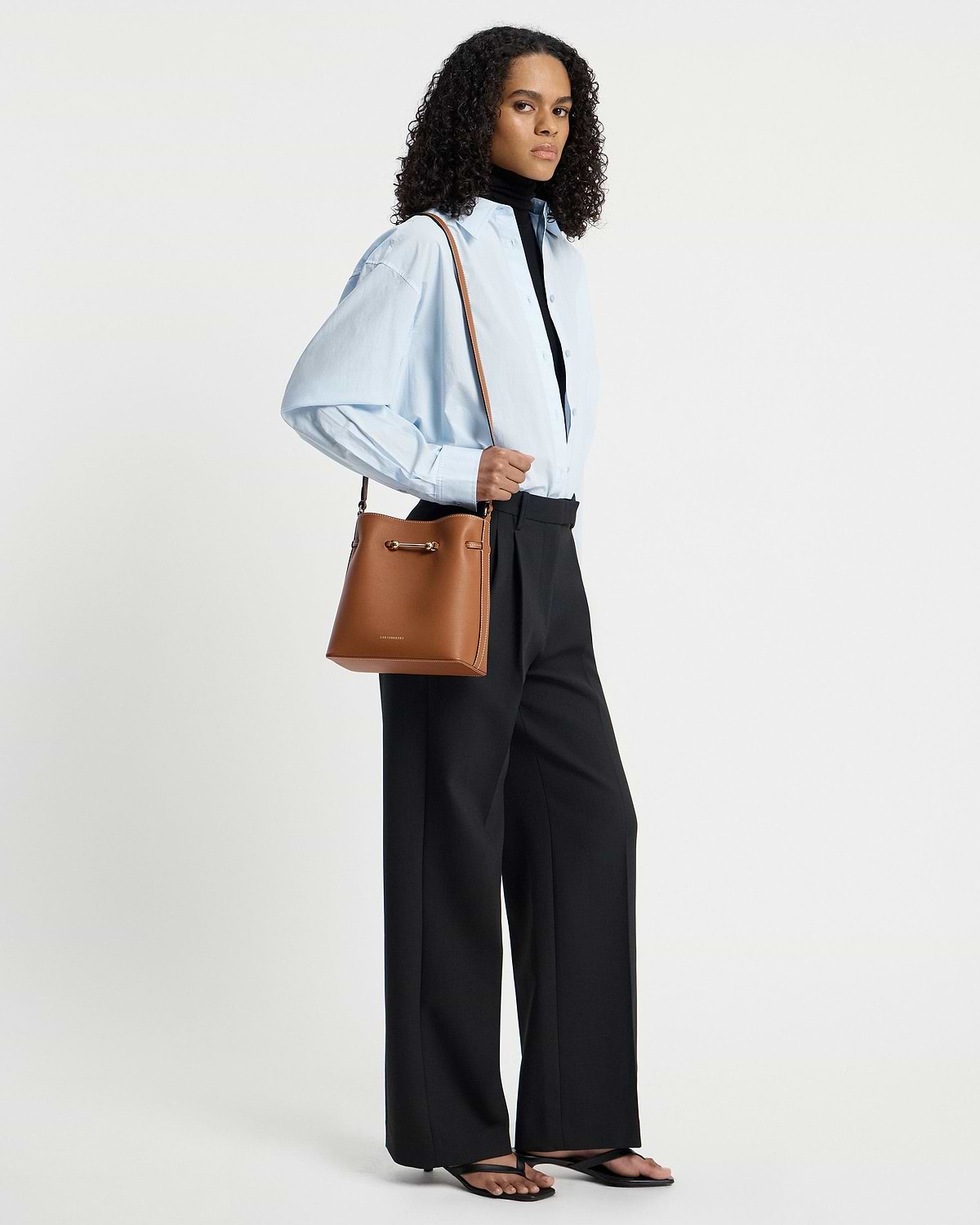 Model wearing chestnut Corda bucket bag over shoulder with light blue shirt.