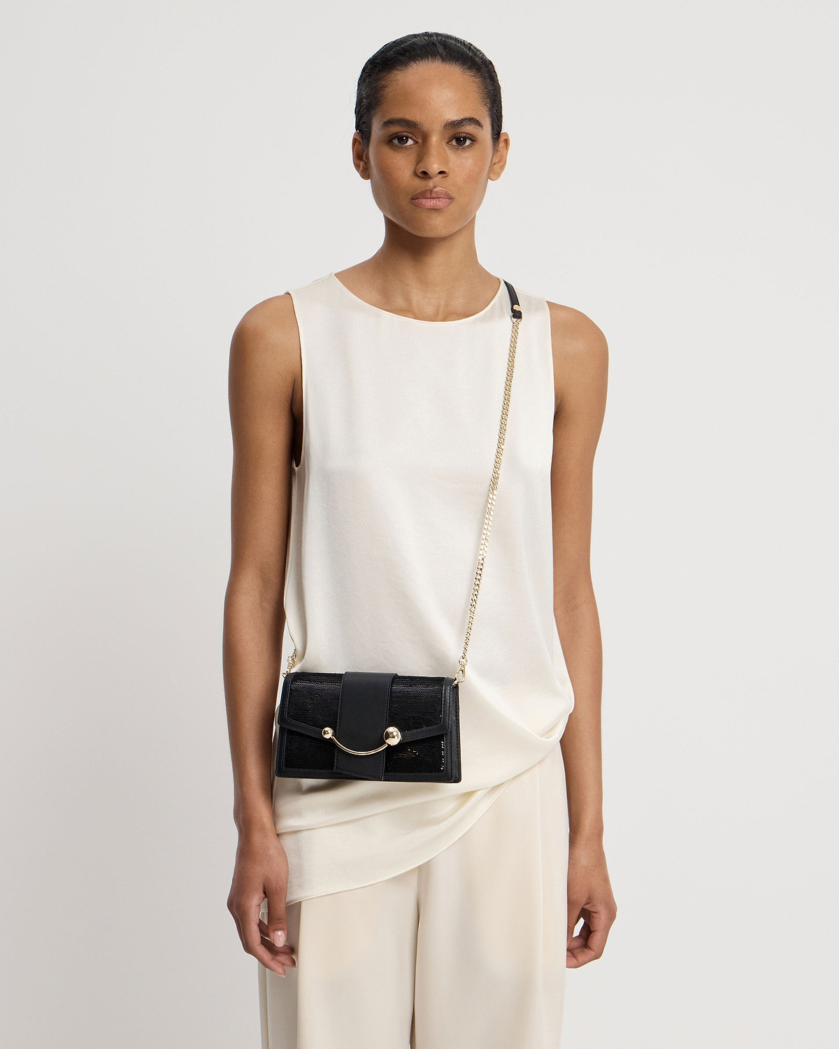Model wearing cream sleeveless top with black sequinned crescent bag on gold chain.