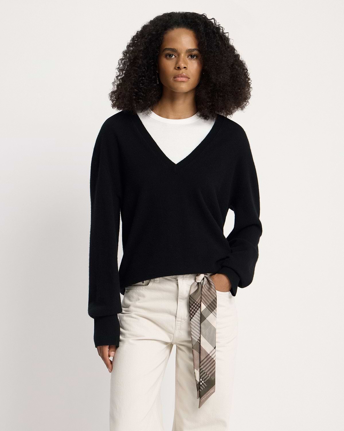 Model wearing a black V-neck sweater and white trousers with green tartan silk skinny scarf.
