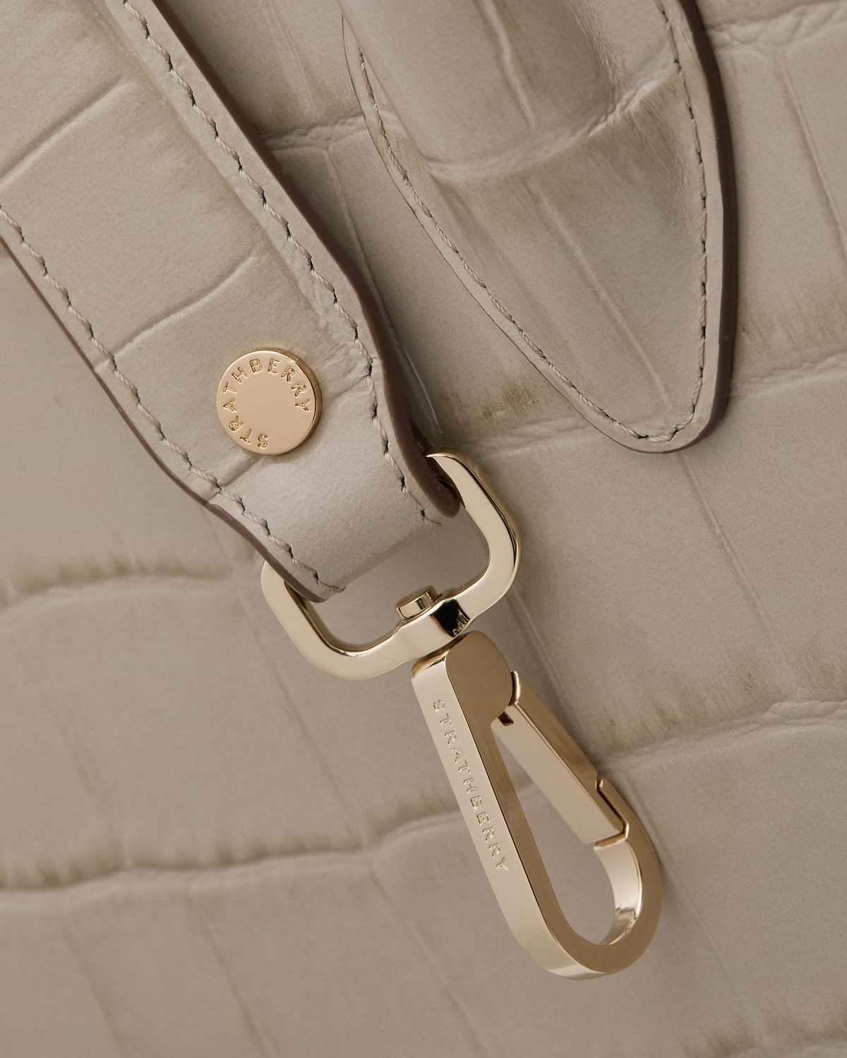 Close-up of croc-embossed midi tote strap with gold hardware engraved Strathberry