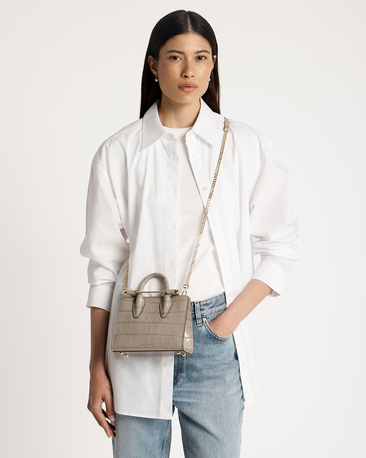 Model wearing white shirt and jeans carrying croc nano tote with gold chain strap.