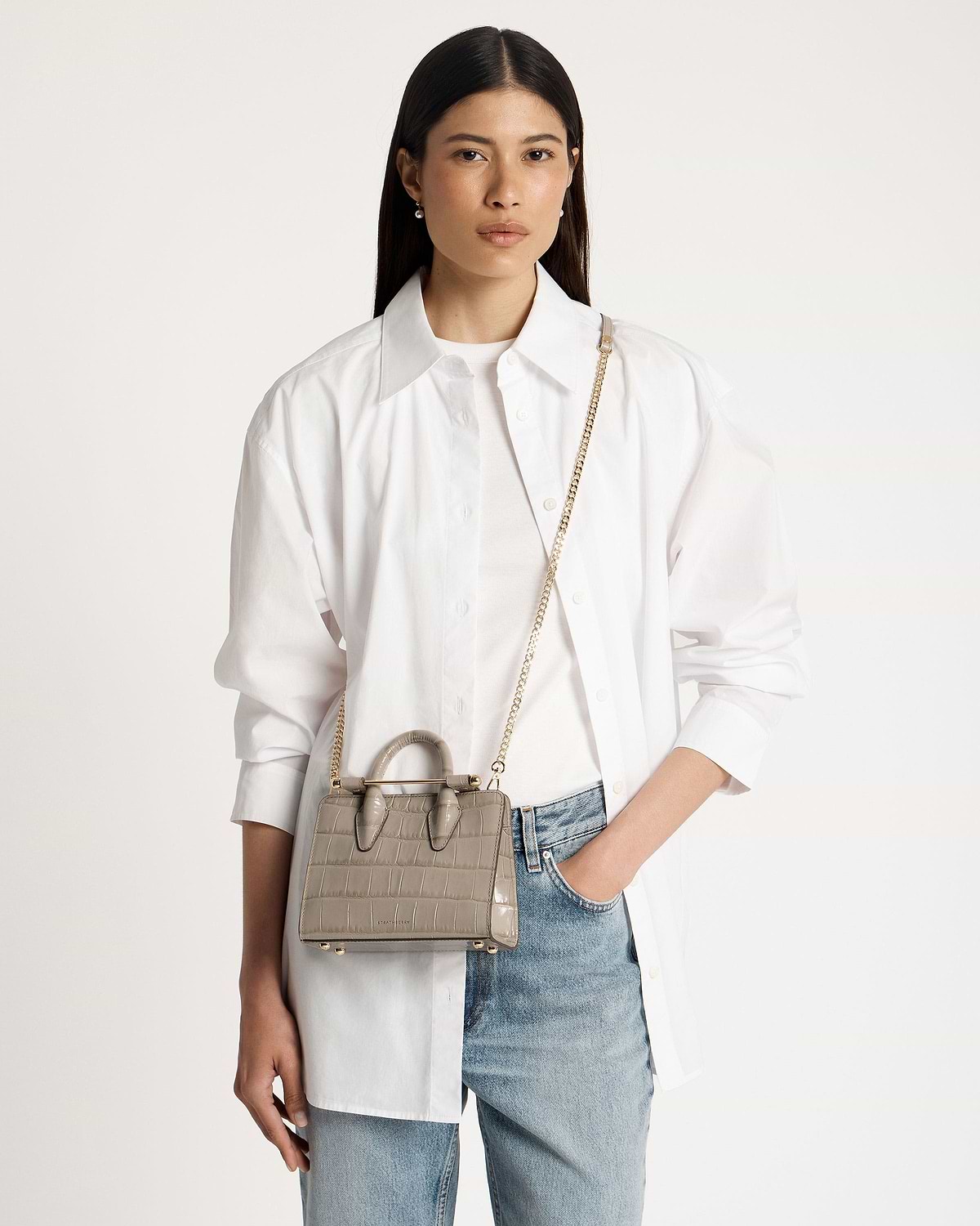 Model wearing white shirt and jeans carrying croc nano tote with gold chain strap.